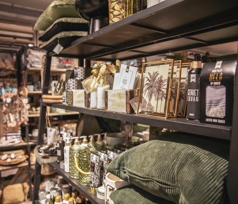 Winkelstelling met woonaccessoires zoals kussens, geurkaarsen, decoratieve lijsten, flessen en opbergmanden.