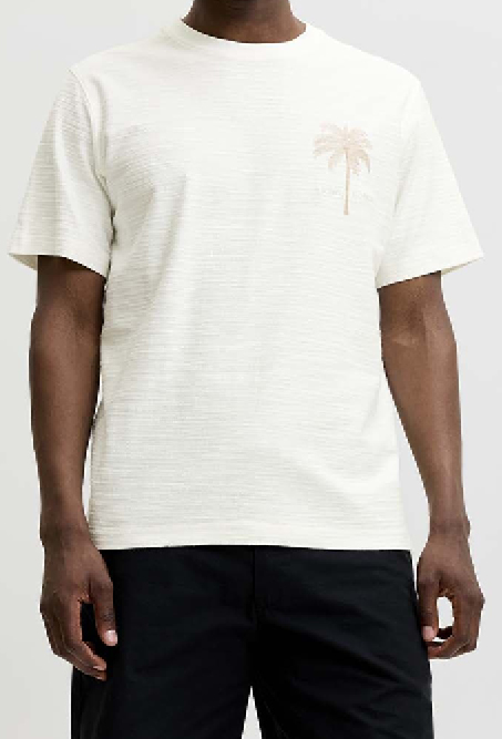 Persoon draagt een licht crèmekleurig linnen T-shirt met korte mouwen en een subtiel palmboommotief op de borst. Gecombineerd met een donkere broek tegen een lichtgrijze achtergrond.