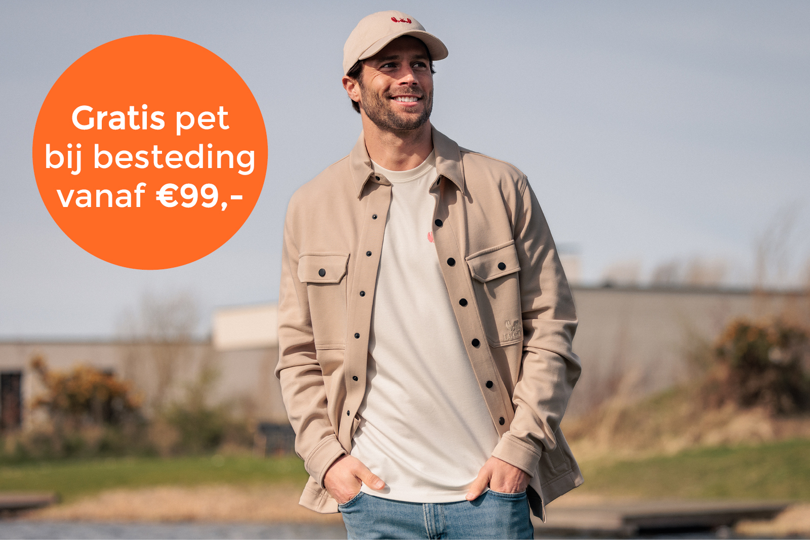 Man draagt een beige pet, lichtbruin overshirt en T-shirt terwijl hij buiten glimlachend poseert met zijn handen in de zakken. Rechts staat een oranje cirkel met de tekst: “Gratis pet bij besteding vanaf €99,-”. Onderaan staat het logo en de naam “Luctor”