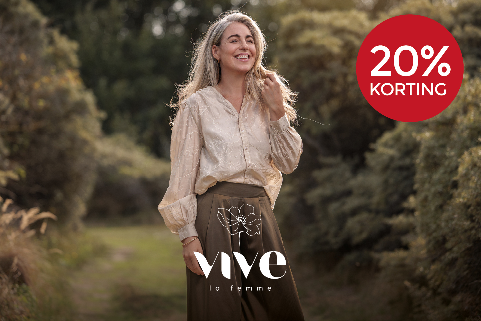 Vrouw in een lichte blouse en donkerbruine broek met 20% korting op Vive La Femme.